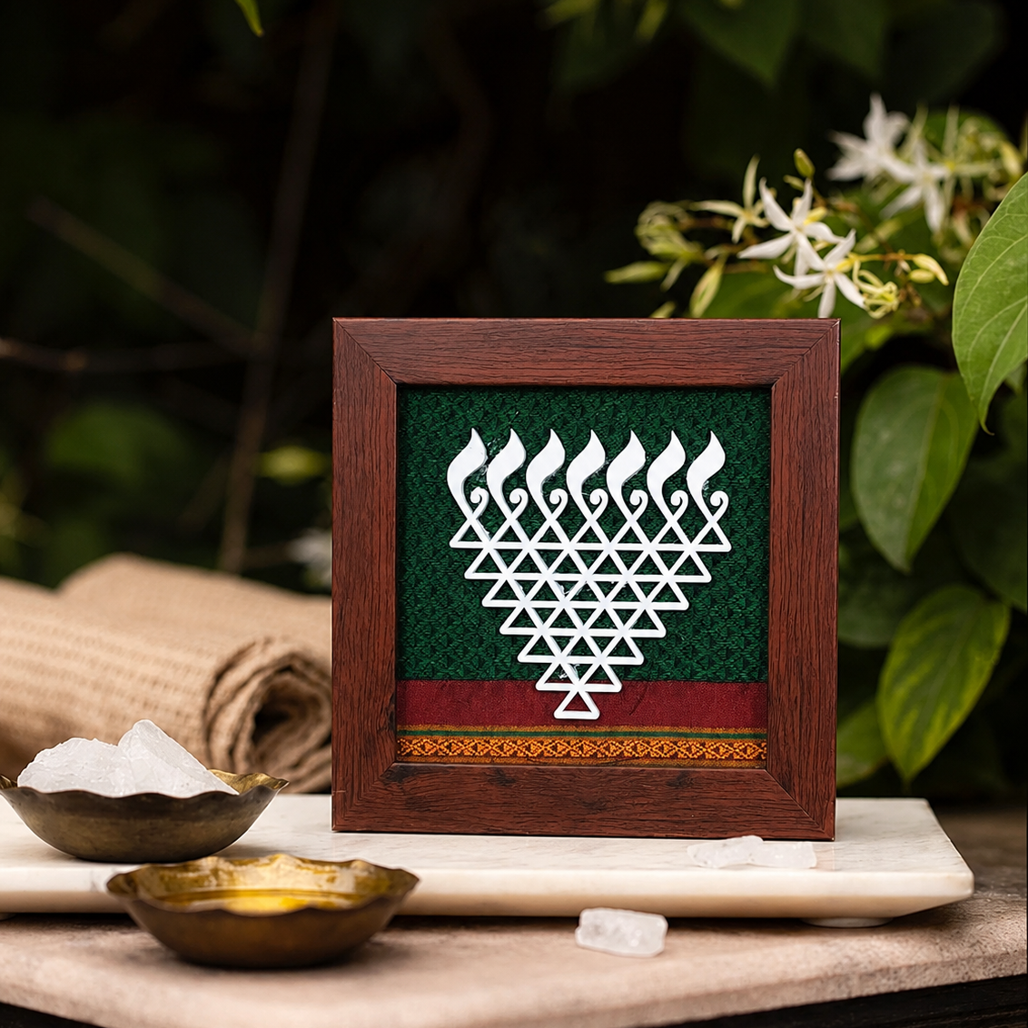 Decorative framed artwork with a geometric design on a wooden table with bowls and flowers.